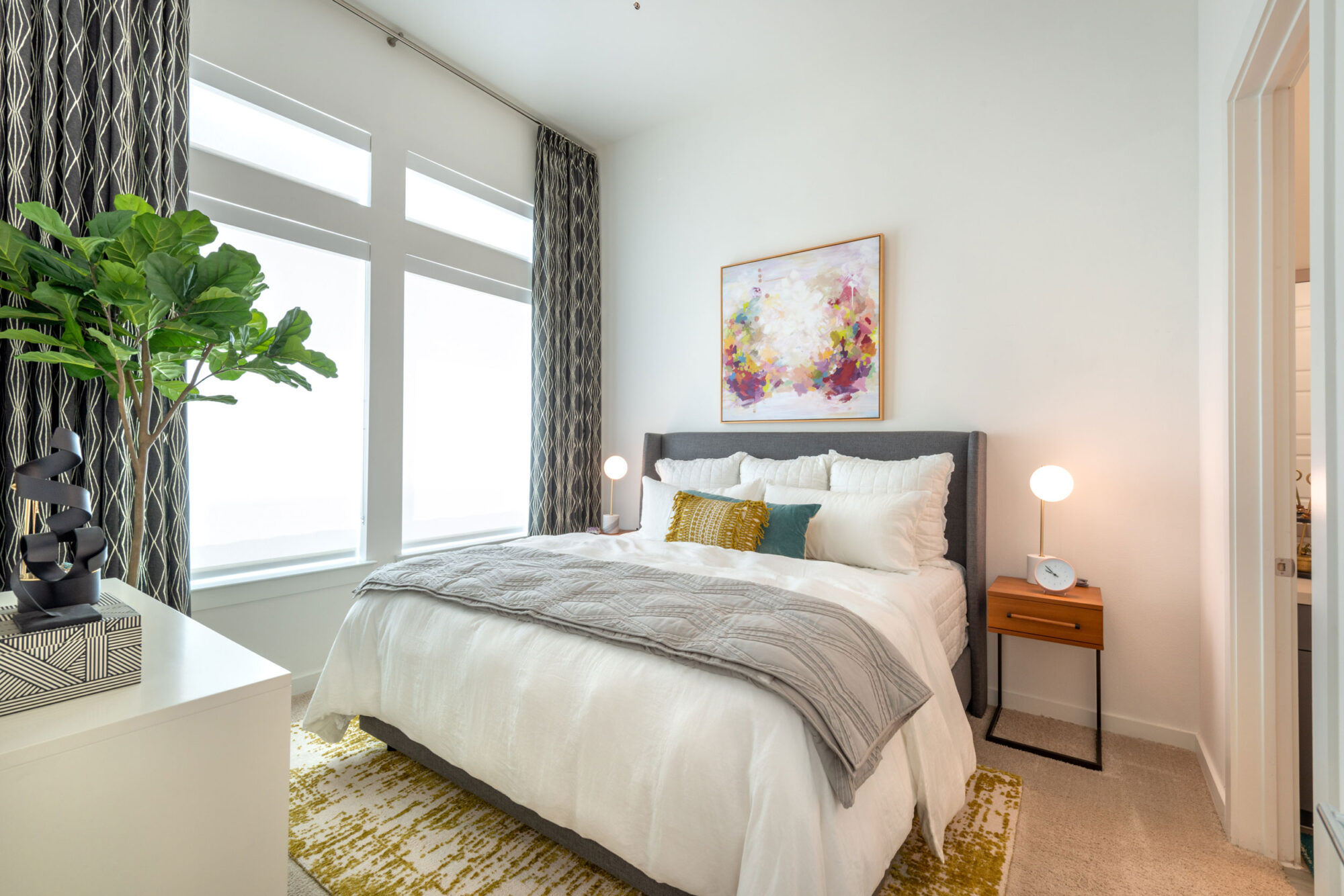 Bedroom with plush carpeting, ceiling fan, large windows for natural light and door to private bathroom