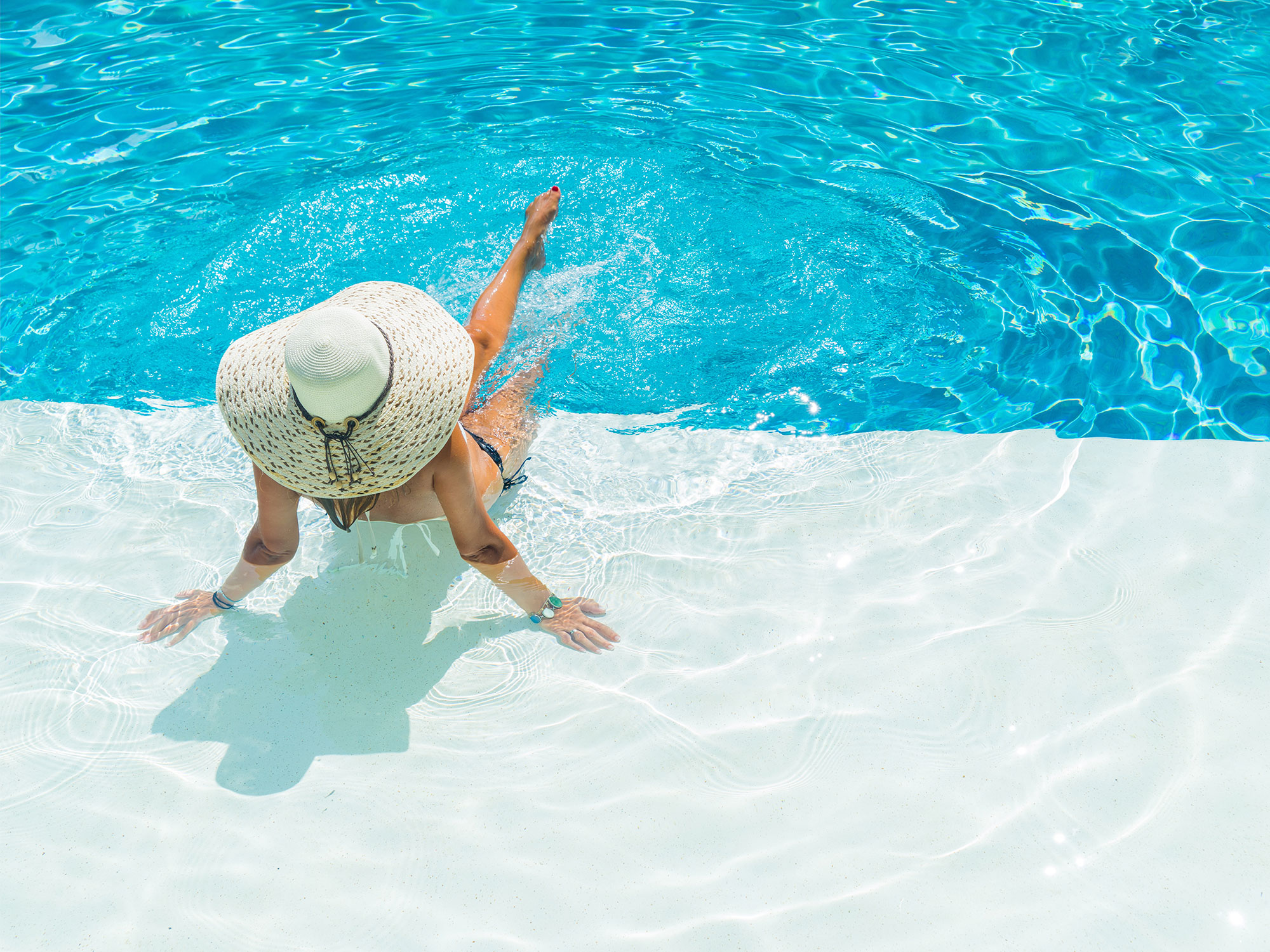 Woman in large hat sitting on tanning ledge of pool